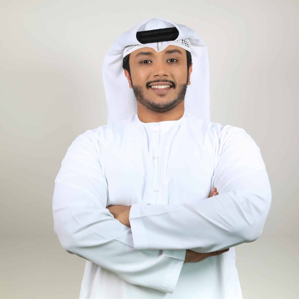 Confident Middle Eastern man smiling in traditional attire with crossed arms, studio portrait.